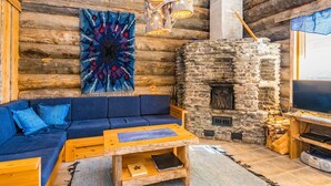 A cozy log cabin interior with a blue sofa, a wooden coffee table, a stone fireplace, and a colorful abstract wall hanging. - Rinnekieppi 2 by Interhome (Kuusamo)