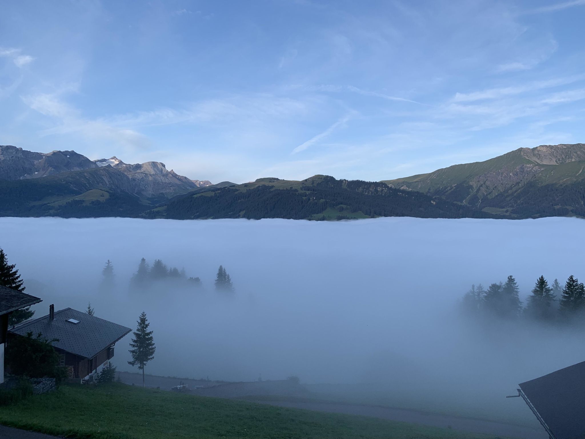 A mountain landscape with a house in the foreground and a lake with a misty foreground.