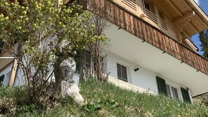 Une maison en bois à deux étages, dotée d’un balcon, entourée de verdure et surplombant un ciel dégagé.