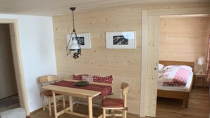Une pièce aux murs lambrés, comprenant une table à manger, des chaises, un lit et deux tableaux encadrés.