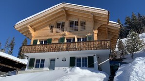 Un chalet en bois à plusieurs étages, doté d’un balcon, entouré d’arbres couverts de neige et surplombant un ciel bleu clair.