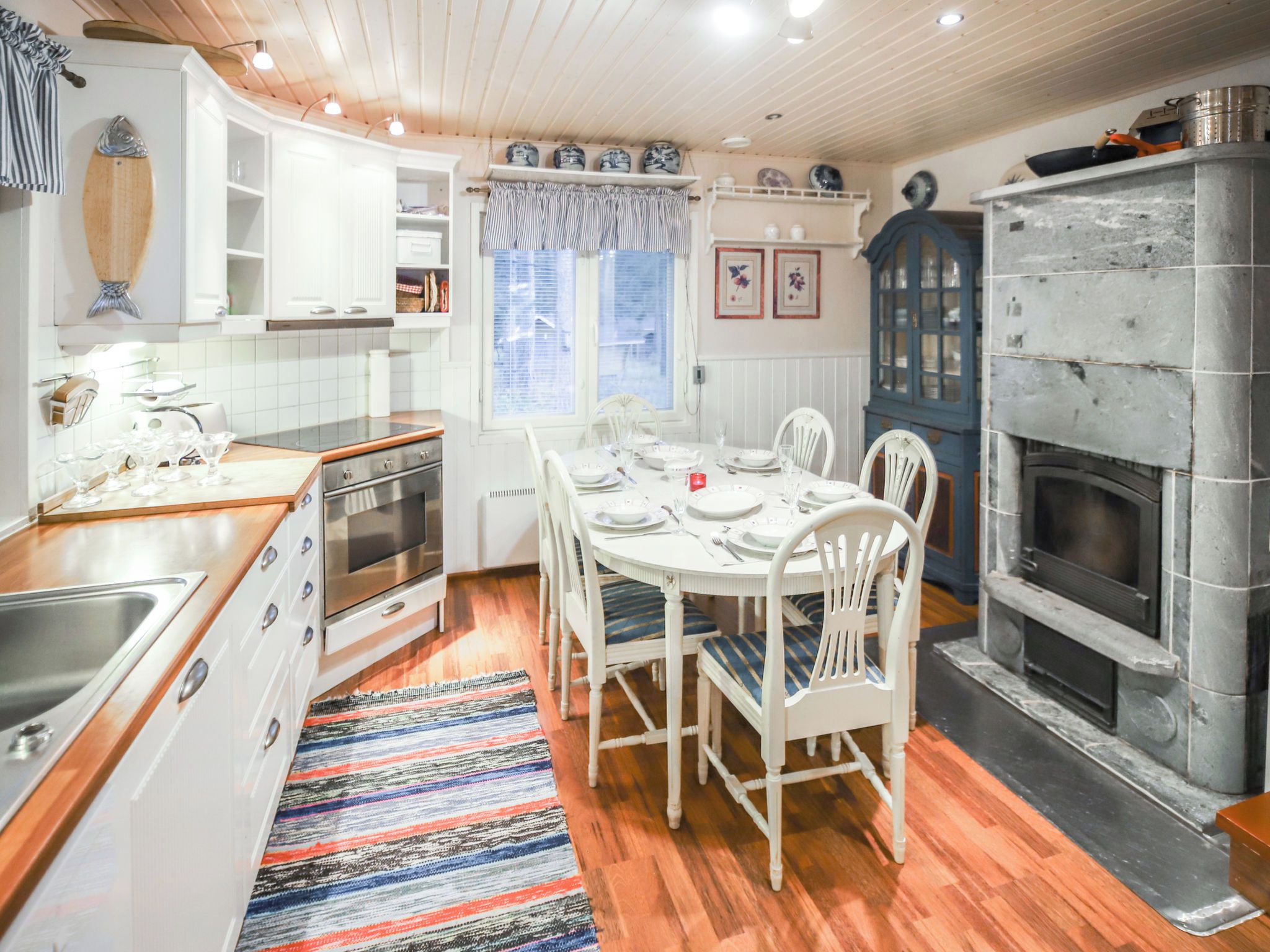A kitchen with white cabinets, a stove, a dining table set for four, and a stone fireplace.