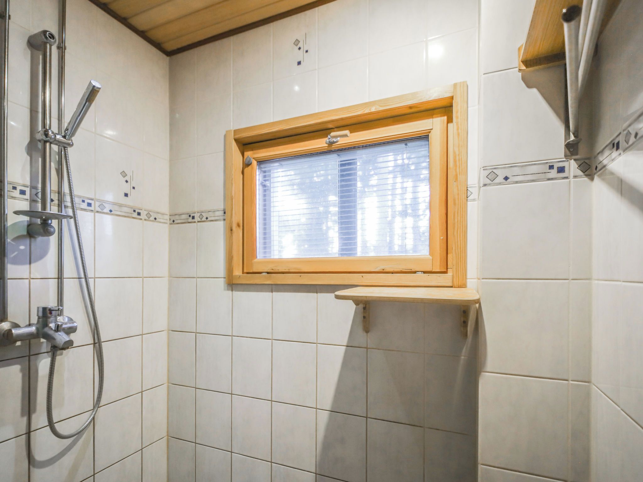 A shower area with a window, tiled walls, and a wooden shelf.