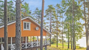 A wooden cabin with a porch and deck, surrounded by tall trees and a clear sky.