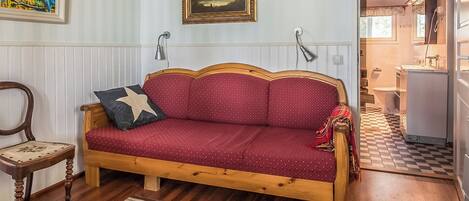 A cozy room with a wooden sofa, a chair, a patterned rug, and a painting on the wall.