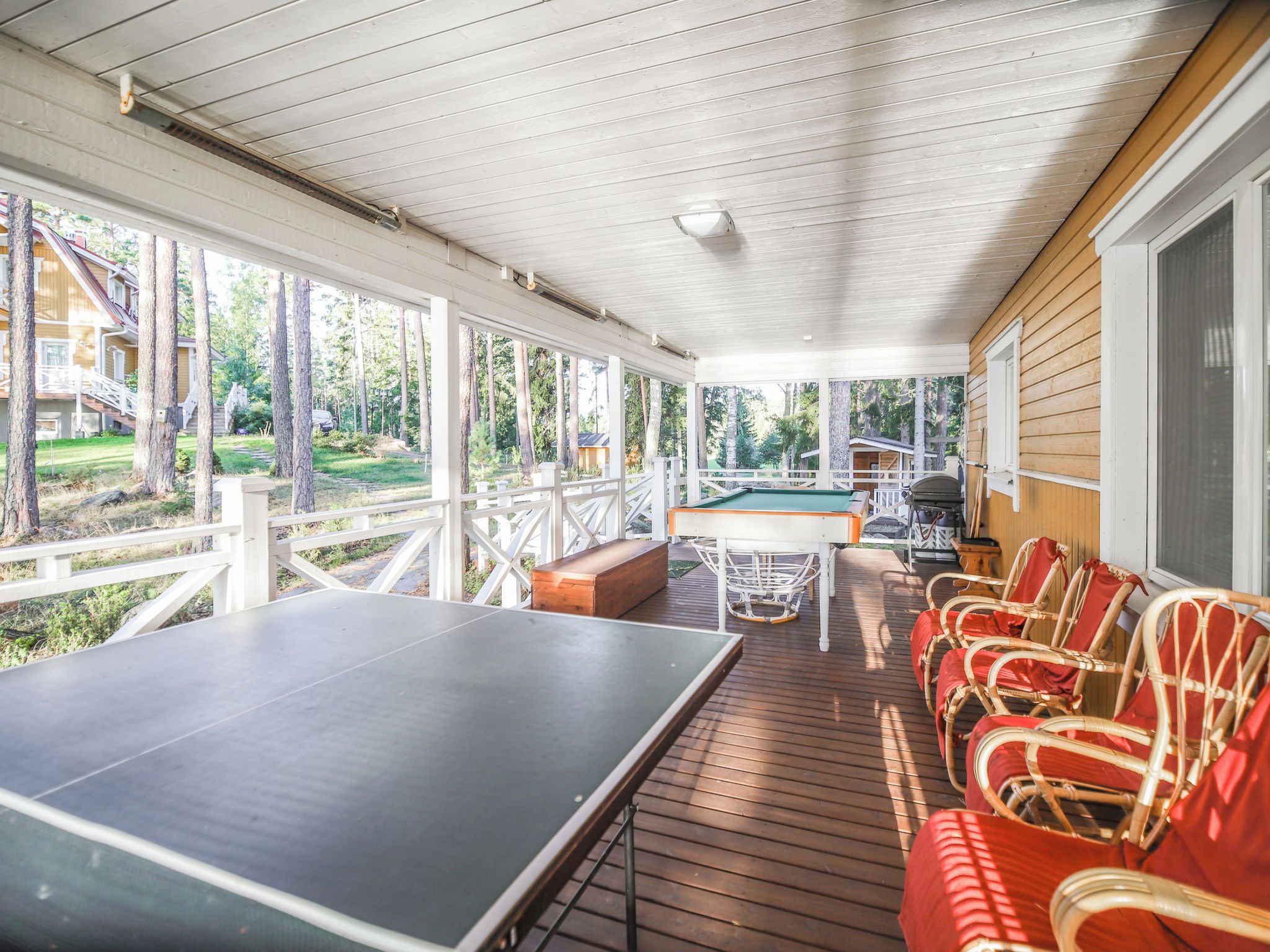 A covered outdoor area with a ping pong table, a pool table, and wicker chairs.