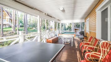 A covered outdoor area with a ping pong table, a pool table, and wicker chairs.