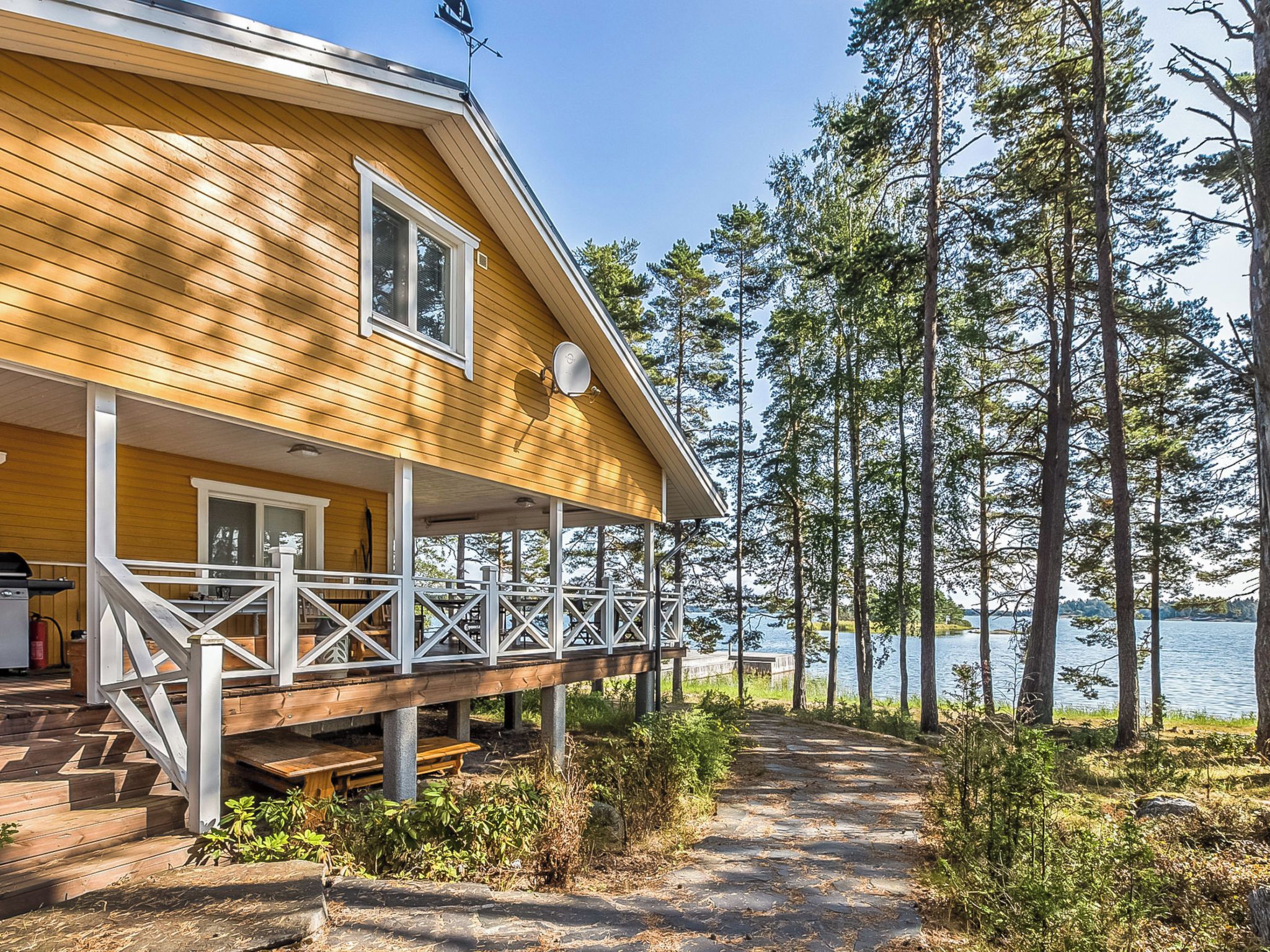 Une maison en bois dotée d’un porche abrité, d’une terrasse et offrant une vue sur un lac entouré d’arbres.