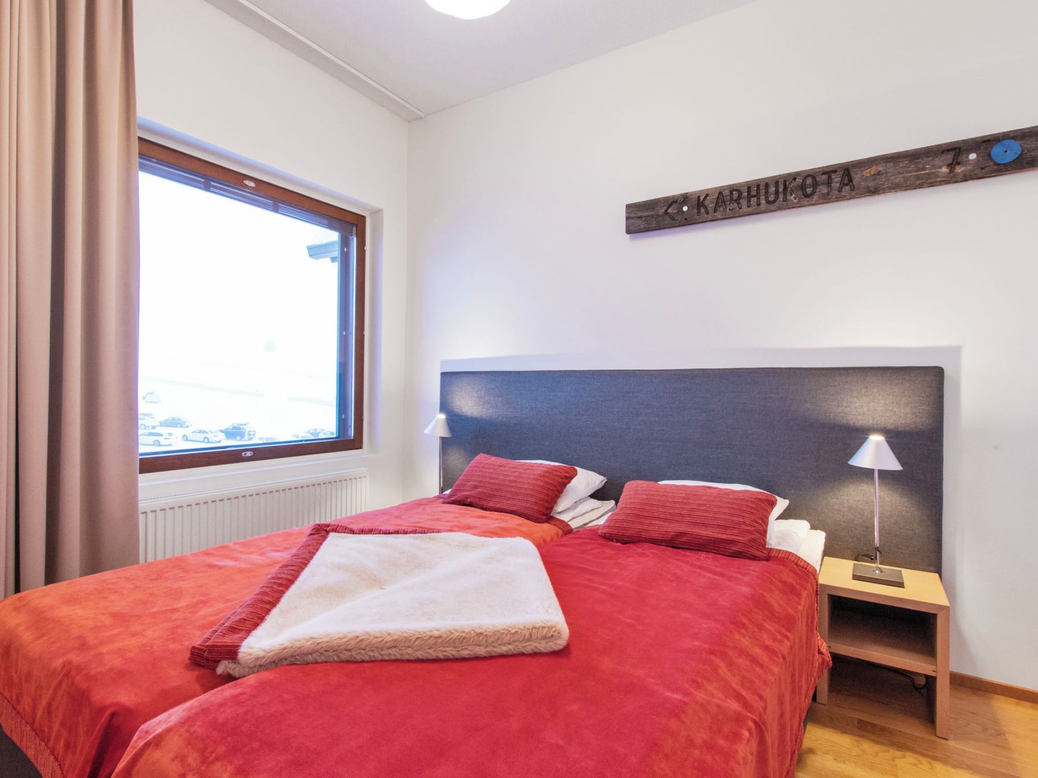 A bedroom with a bed, two bedside tables, a lamp, a window, and a wall-mounted sign.