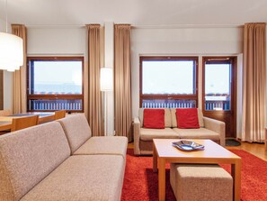 Et hotelværelse med sofa, et lille bord, et vindue med udsigt og gardiner.