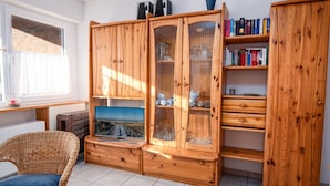 Ein Zimmer mit einem Holzschrank, einem Korbstuhl und einem Fernseher, der eine schöne Aussicht zeigt.