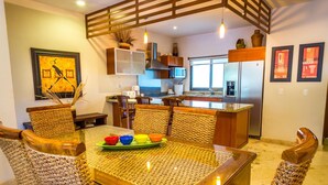 A modern kitchen with stainless steel appliances, a dining area with a glass table, and a wooden ceiling. - Luxury 3 bedroom Condo in Paseo del Sol by BRIC (Playa del Carmen)
