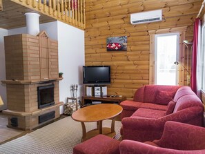 Uma sala de estar com lareira, televisão, sofá e teto de madeira.