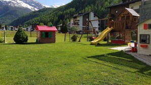 Un'area giochi con uno scivolo, una piccola casetta di legno e case in zona montana.