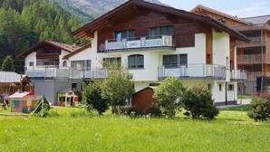 Un edificio a più piani con balconi, circondato da un'area verde e montagne sullo sfondo.
