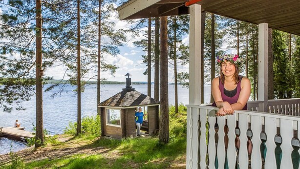 Eine Holzterrasse mit Geländer, die auf einen See blickt, eine kleine Holzhütte und ein Steg, auf dem jemand fischt.