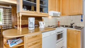 Eine kleine Küche mit Holzschränken, einem eingebauten Herd, einer Kaffeemaschine und einem Spülbecken.