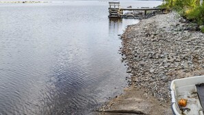 Ein ruhiger See mit einer anlegenden Mole, umgeben von einer felsigen Uferlinie und etwas Grün.