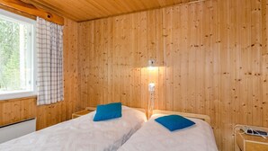 Ein Zimmer mit Holzvertäfelung, zwei Betten mit blauen Kissen, ein Nachttisch mit Lampe und ein Fenster mit Vorhängen.