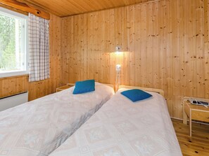 A room with wooden walls, a bed with patterned bedding, a bedside lamp, and a window with curtains. - Mäntylä by Interhome (Nurmes)