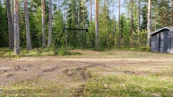 Metsäinen alue, jossa on leikkikeinu ja pieni varasto.