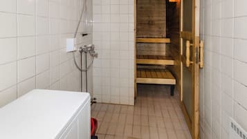 A small, tiled bathroom with a shower, a wooden bench, and a white washing machine.