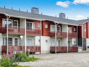 A multi-story residential building with balconies, a gravel driveway, and a clear sky.