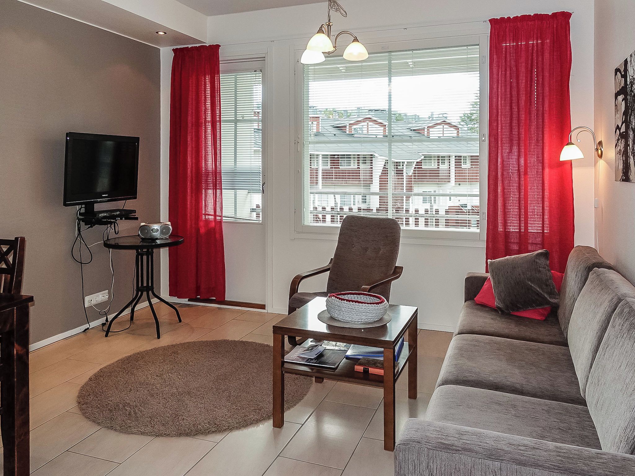 A living room with a sofa, armchair, television, and a table with a basket and books.