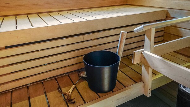 Eine Sauna mit Holzbänken und einem schwarzen Eimer.