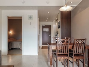 Moderni hotellihuone, jossa on sänky, ruokailutila puutuoleineen ja pöytineen sekä kattovalaisin.