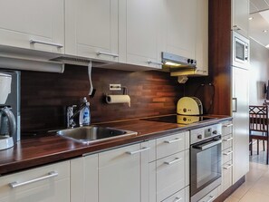 Cozinha moderna com armários brancos, pia de aço inoxidável, forno embutido e micro-ondas.