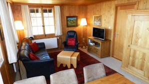 L'interno accogliente di una baita con arredamento in legno, un divano, una televisione e un tavolo da pranzo.