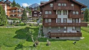 Un edificio a più piani in legno con balconi, immerso nel verde e con montagne sullo sfondo.