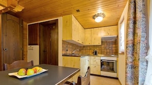Una cucina compatta con mobili in legno, un lavello e un piano cottura. C'è un tavolo da pranzo con sedie e un piatto di frutta.
