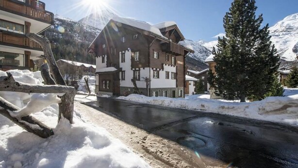 Un edificio innevato con facciata in legno, cielo sereno e una montagna sullo sfondo.