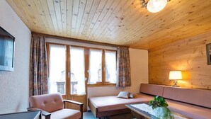 Una stanza accogliente con soffitto in legno, un divano, una poltrona, un tavolino con una pianta e una lampada.