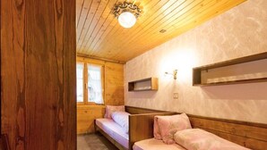 Una stanza accogliente con pareti in legno e soffitto a falde. Sono presenti due letti singoli con biancheria rosa e un piccolo ripiano sopra uno dei letti.
