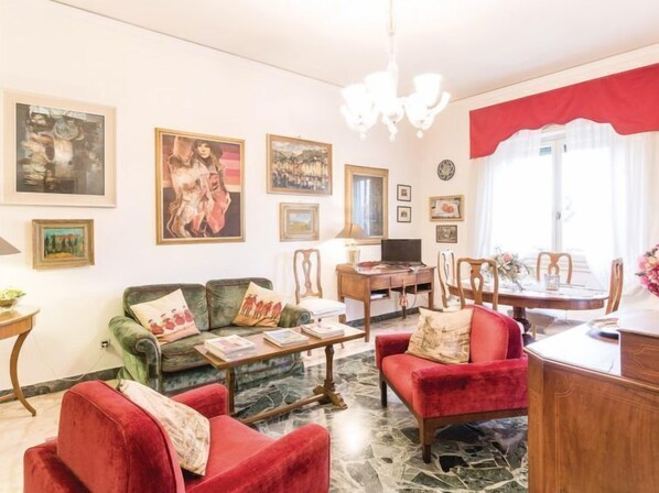 A living room with a green sofa, red armchairs, a wooden coffee table, and a dining area with a table and chairs. - La Torretta by Interhome (Florence)