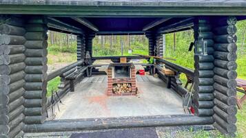 Eine Blockhütte mit einem zentralen Kamin, umgeben von einer Holzterrasse und einem Metallgeländer.
