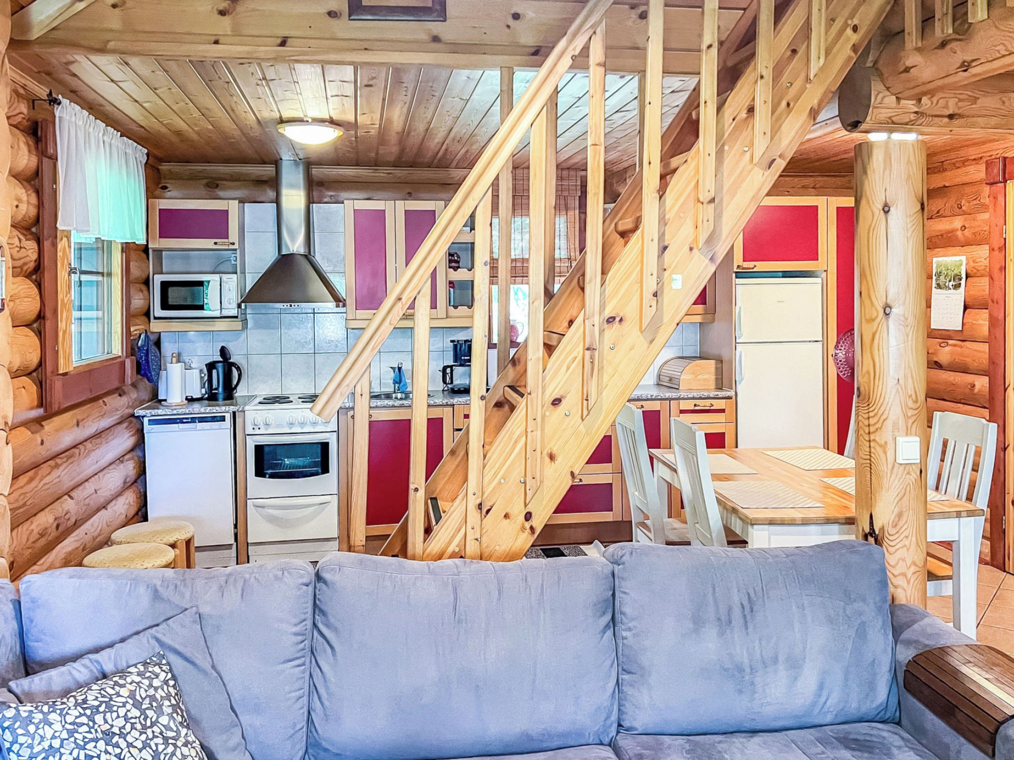 Ein Blockhaus-Innenraum mit einer Holztreppe, einer Küche, einem Essbereich und einem grauen Sofa.