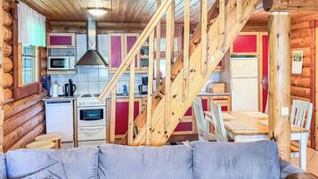 Ein Blockhaus-Innenraum mit einer Holztreppe, einer Küche, einem Essbereich und einem grauen Sofa.