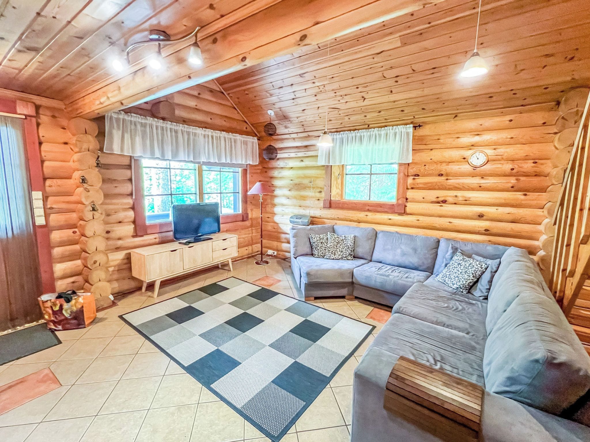 A log cabin interior with a sofa, television, and a checkered rug.