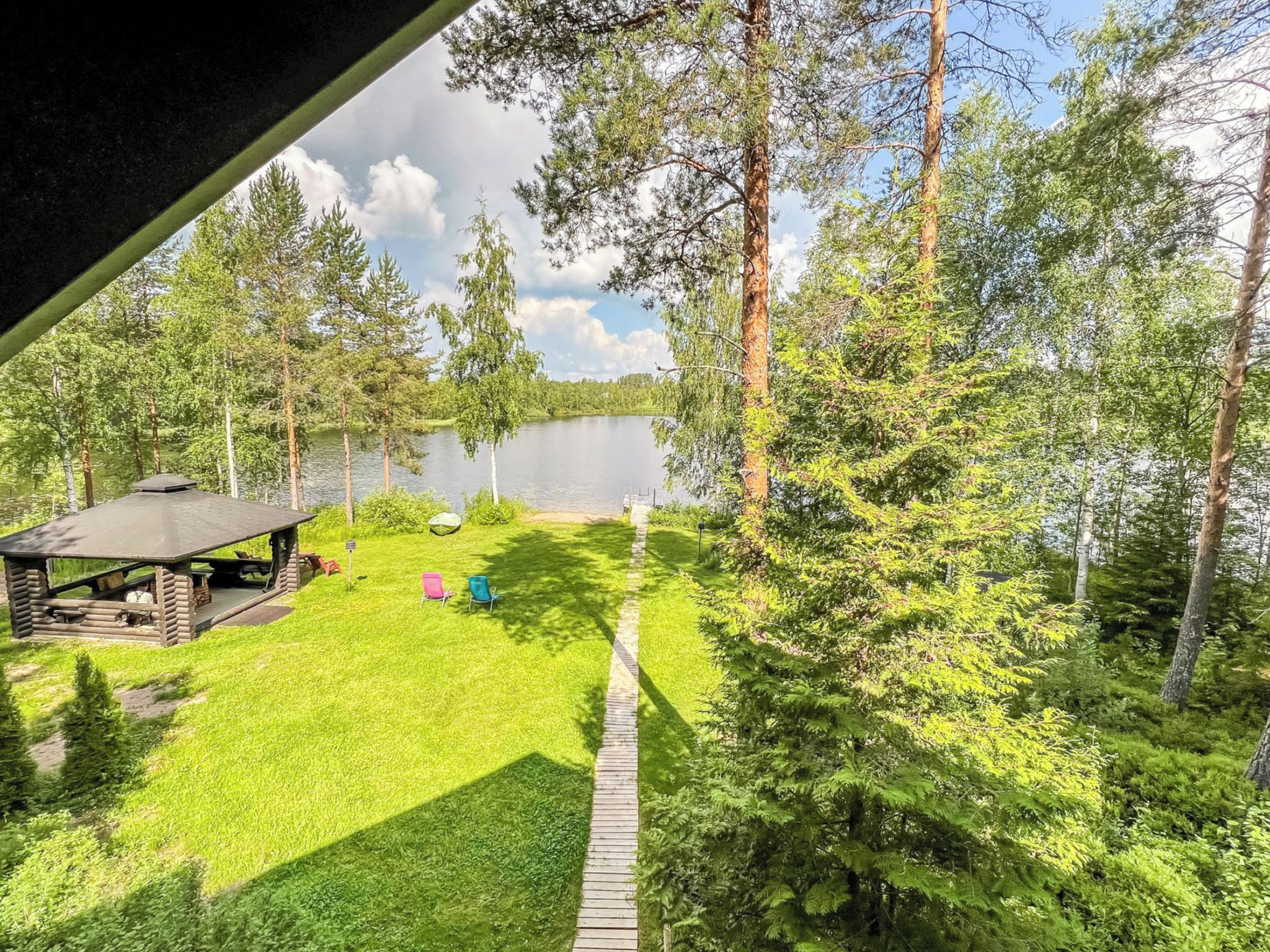 Järven rannalla sijaitseva mökki, jossa on terassi. Mökkiä ympäröi tiheä metsä, ja siitä on kaunis näkymä järvelle.