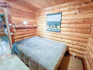 Een houten kamer met een bed, een raam met uitzicht op bomen en een deur naar een andere kamer.