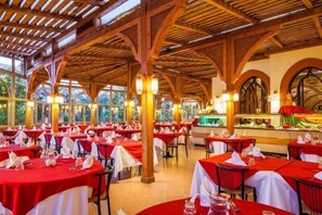 Un restaurant avec des nappes rouges, des poutres en bois et de grandes fenêtres.