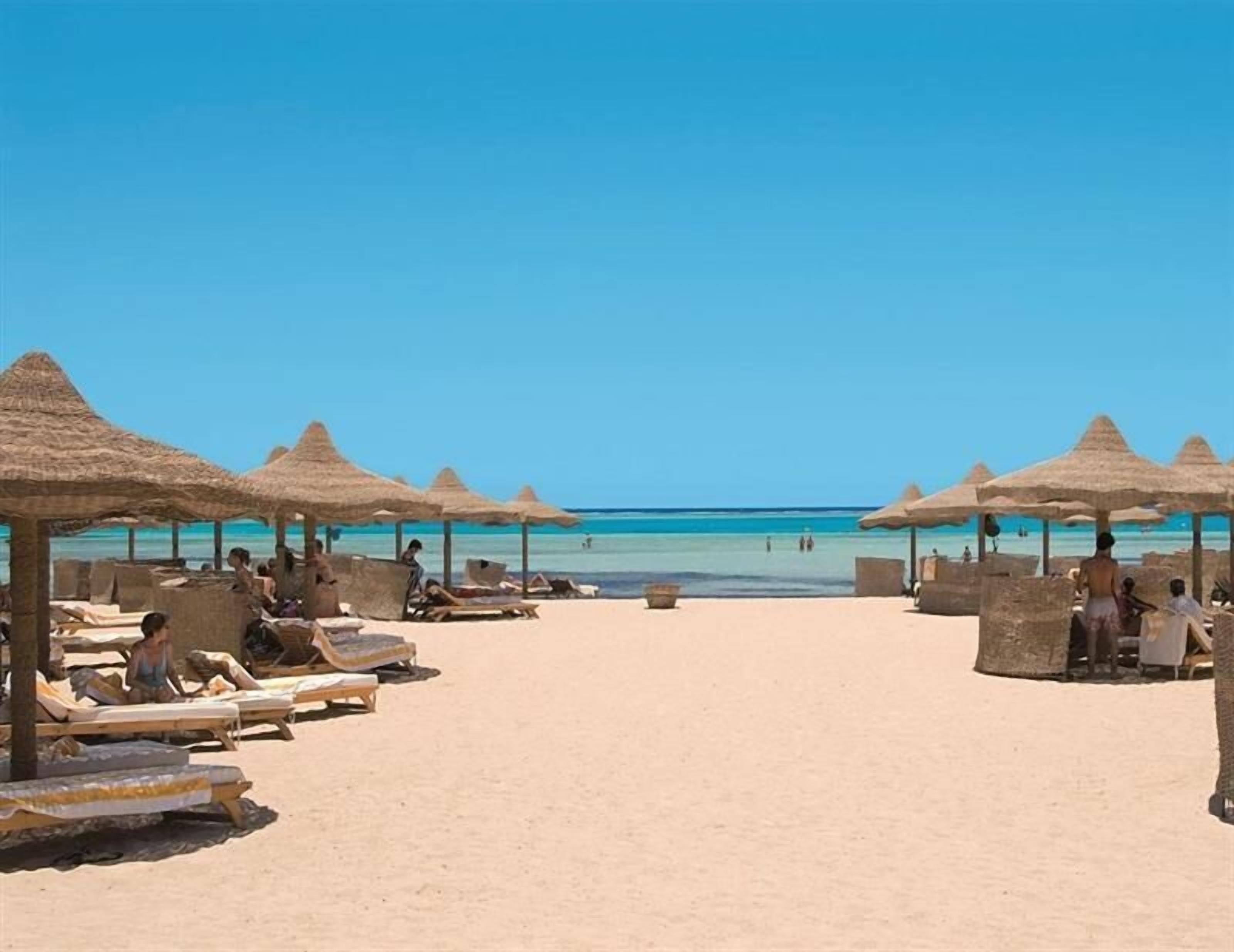 A beach with sun loungers and thatched umbrellas.