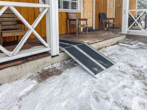 A wooden porch with a metal ramp leading to a door, surrounded by snow.