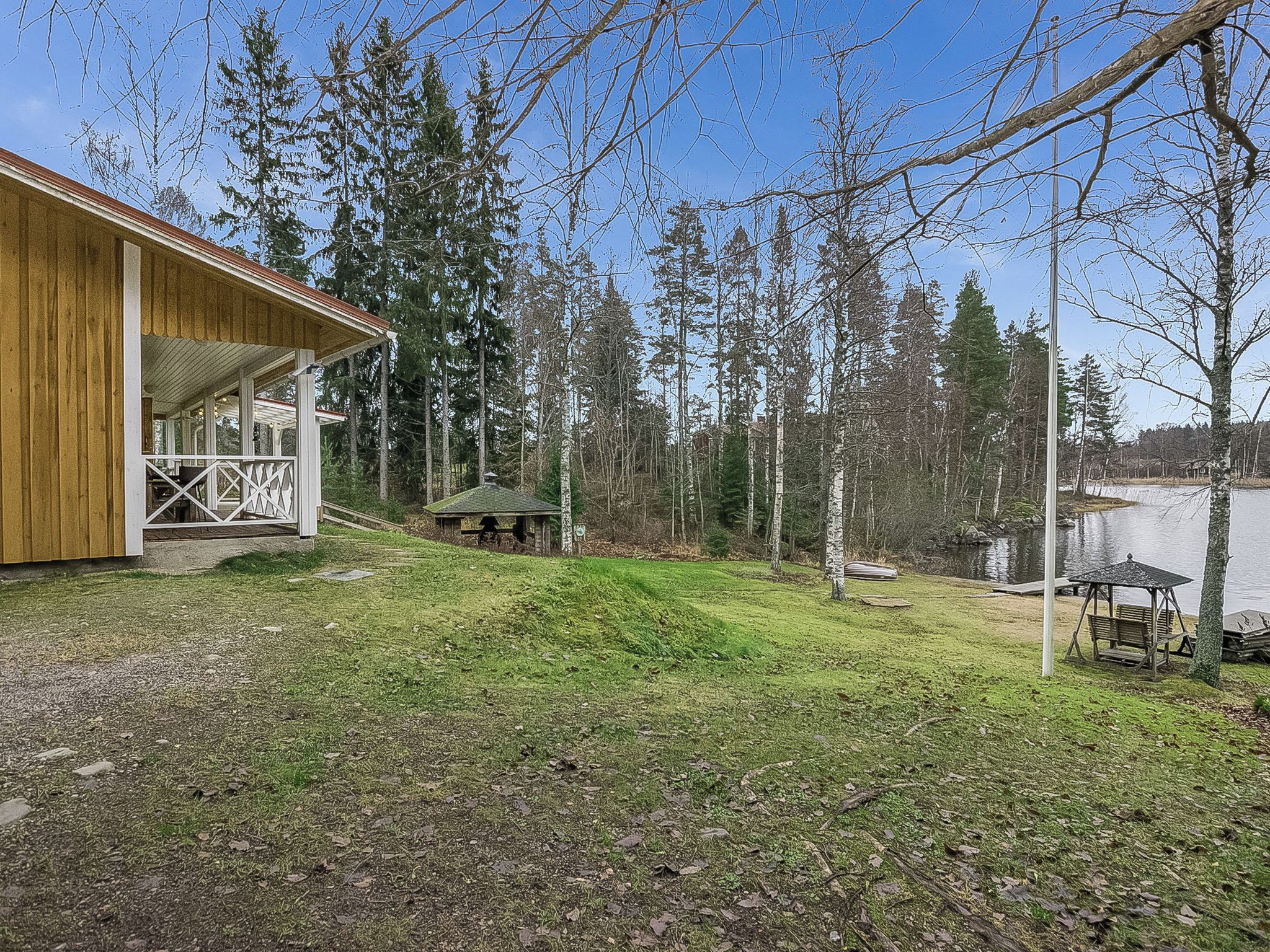 A wooden cabin with a porch, a small shed, and a picnic table by a lake.