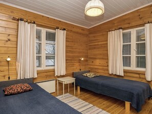 Une pièce aux murs en bois, avec deux lits, une petite table et une lampe.
