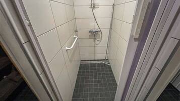 A small, tiled shower stall with a handheld showerhead and a handheld shower control.